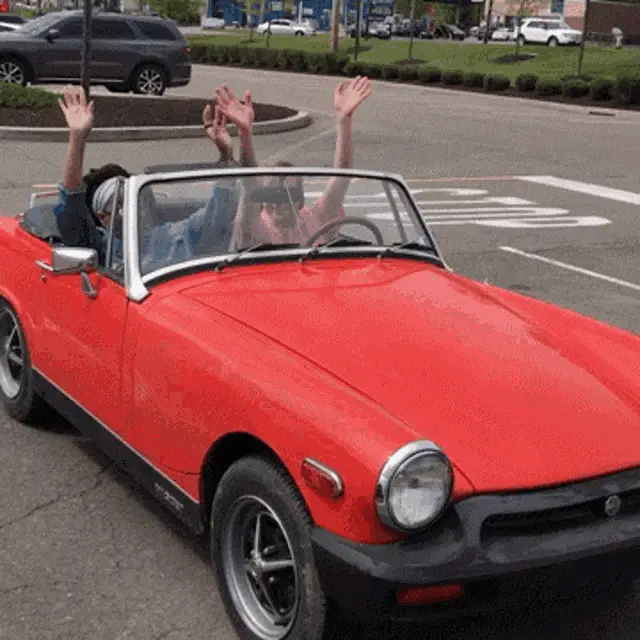 People Waving in a Red MG Convertible Car