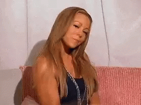 Mariah Carey sitting on a coch, blowing a kiss, and waving